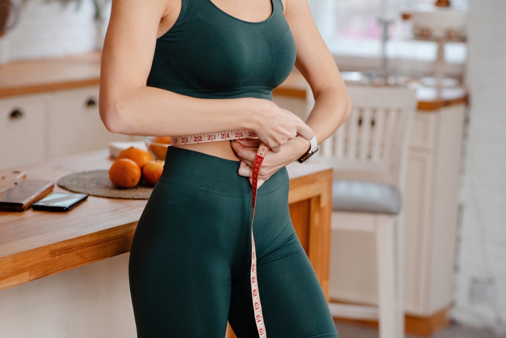 woman in green workout outfit using tape measure to measure her waist